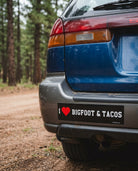 Back of a blue car with a bumper sticker in a forest setting